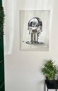 Abstract art piece of a metallic figure on a white wall with plants and a bookshelf.