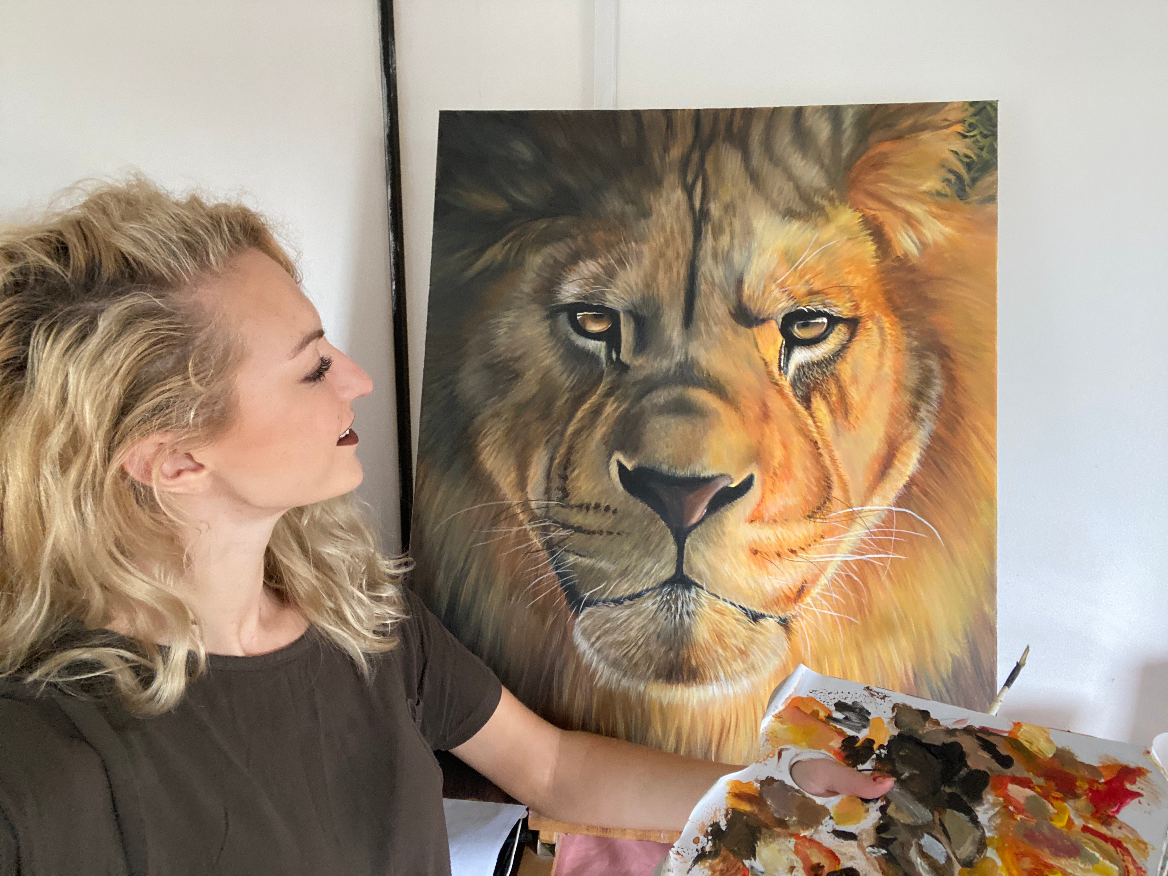 Artist with a completed painting of a lion's face on a white wall